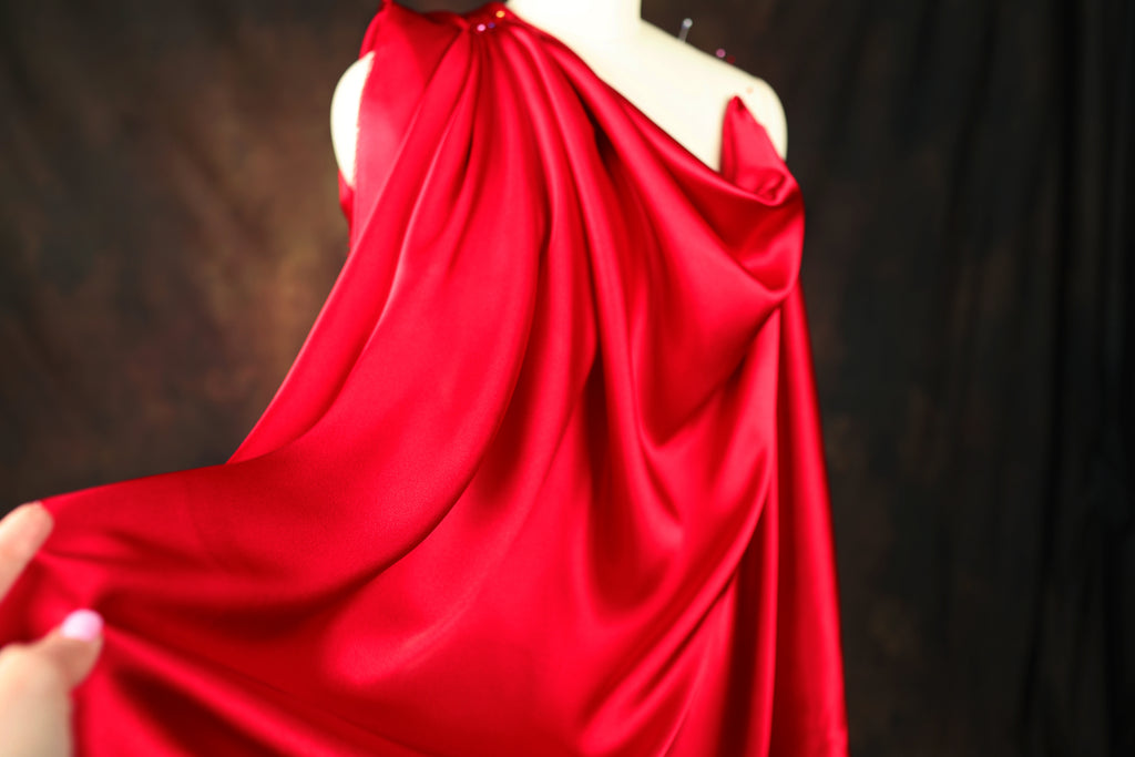 A close-up view of a red satin dress with a draped, flowing silhouette.
