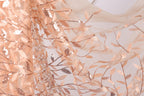 a close-up view of a fabric with a floral pattern, including leaves and branches. The fabric appears to be made of a light-colored material, possibly lace or sheer, with a metallic or sequined appearance. The pattern is intricate and detailed, with the leaves and branches appearing to be made of a shiny material, possibly metallic or sequined. The fabric is spread out, revealing the full extent of the pattern and its details.