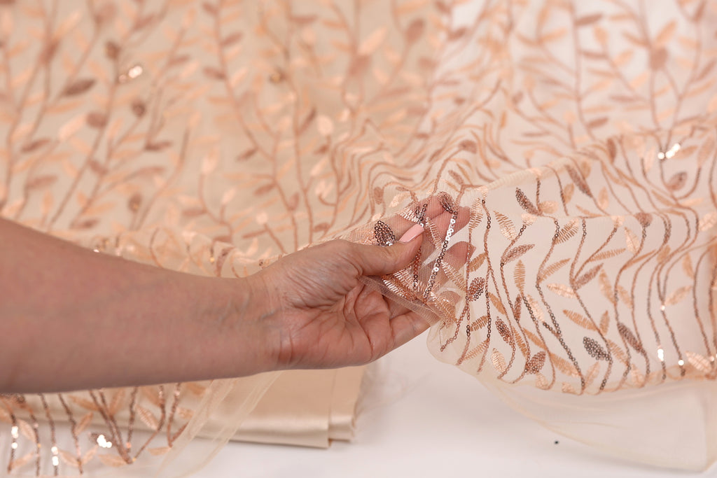 A hand is holding up a piece of fabric with a floral pattern, which appears to be a light pink or peach-colored material.