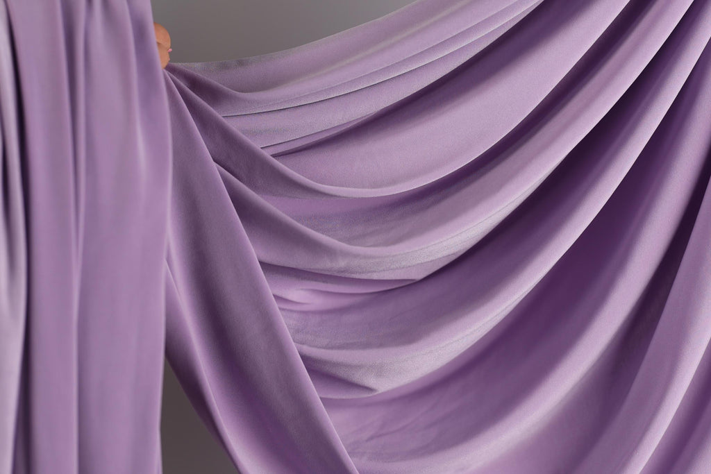 a close-up view of a flowing, purple fabric, possibly a curtain or garment, with a soft, draped appearance.