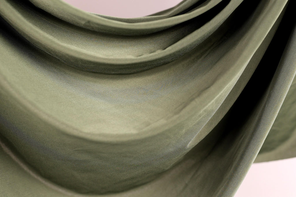 a close-up view of a green fabric, possibly a piece of clothing or a textile. The fabric appears to be folded or draped in a way that creates a sense of movement and texture.