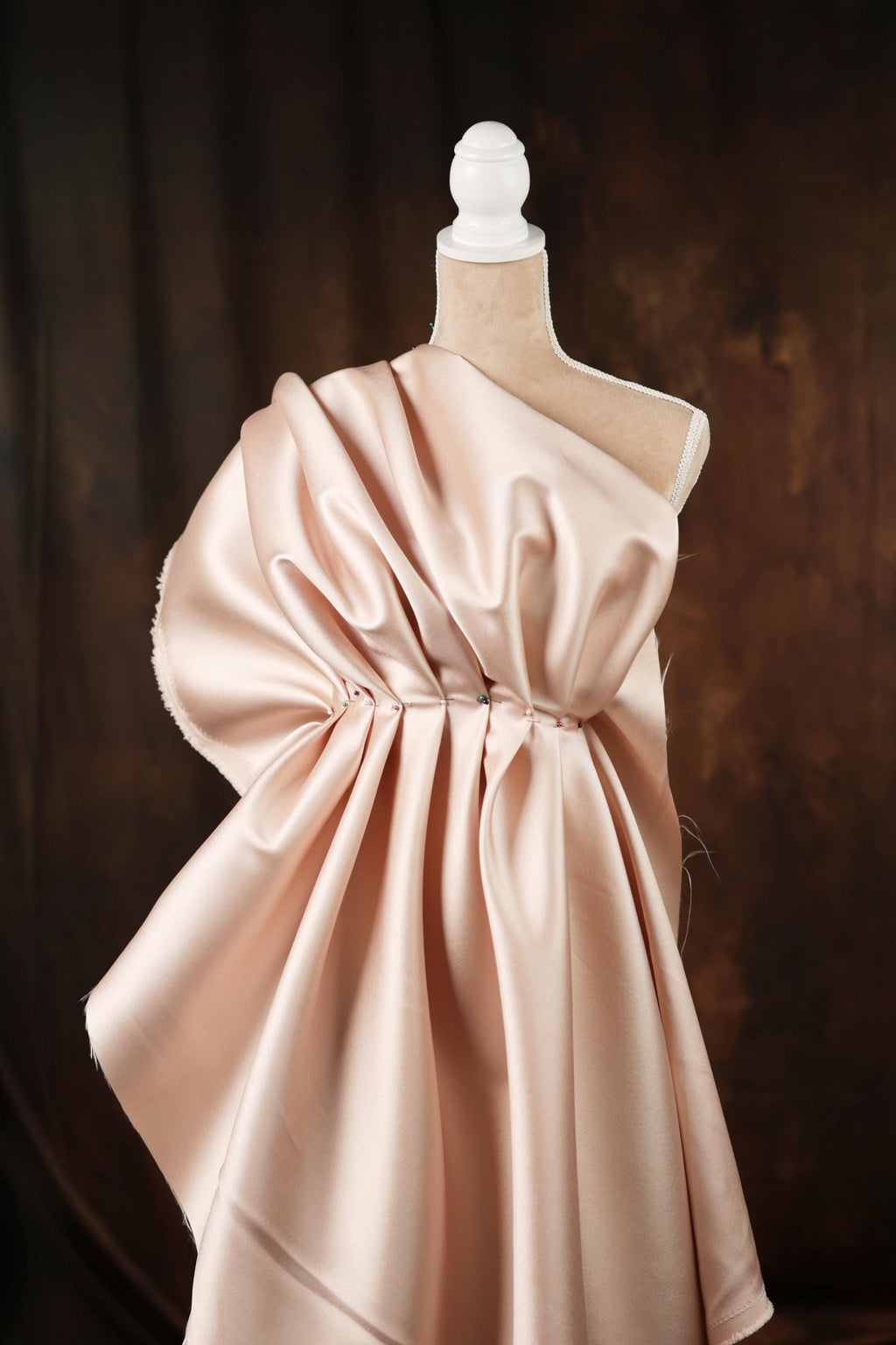 A mannequin wearing a pink satin dress with a ruched waist and a draped skirt.