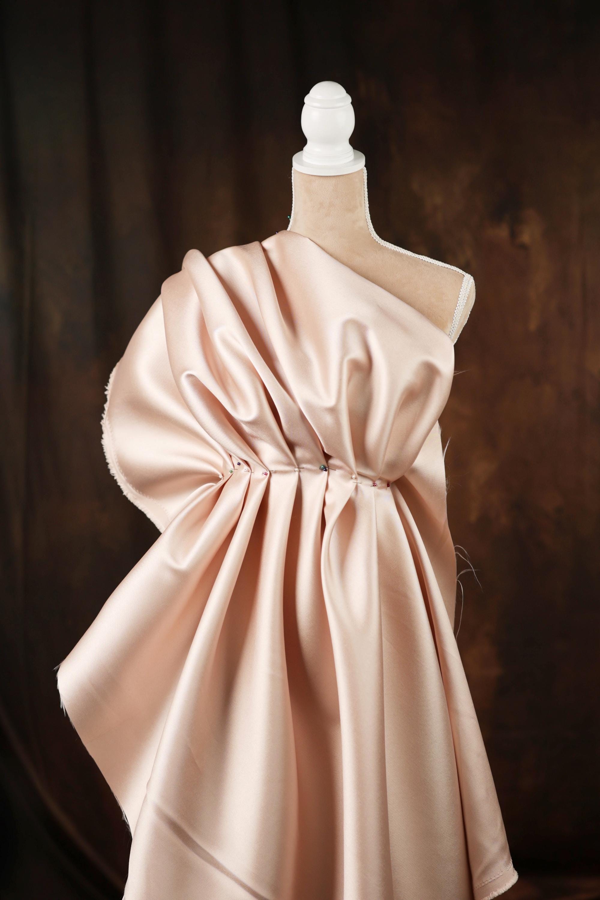 A mannequin wearing a pink satin dress with a ruched waist and a draped skirt.
