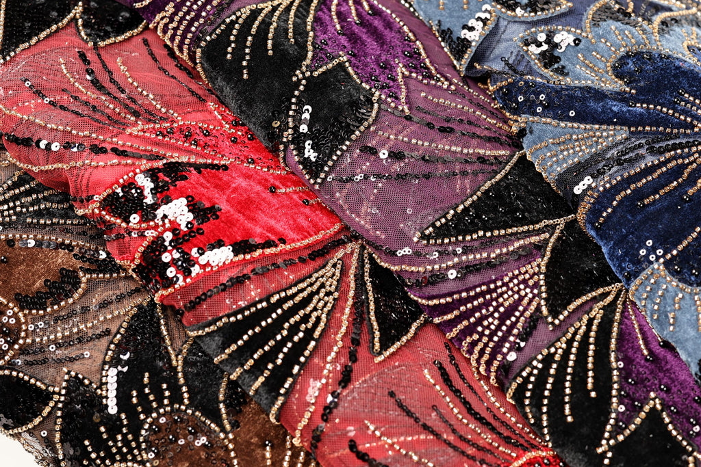 The image is a close-up of a fabric with a vibrant, colorful pattern of sequins and beads. The fabric appears to be a mix of red, black, and purple colors, with the red fabric being the most prominent. The pattern is intricate and detailed, with the sequins and beads creating a visually striking effect.