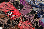 The image is a close-up of a fabric with a vibrant, colorful pattern of sequins and beads. The fabric appears to be a mix of red, black, and purple colors, with the red fabric being the most prominent. The pattern is intricate and detailed, with the sequins and beads creating a visually striking effect.
