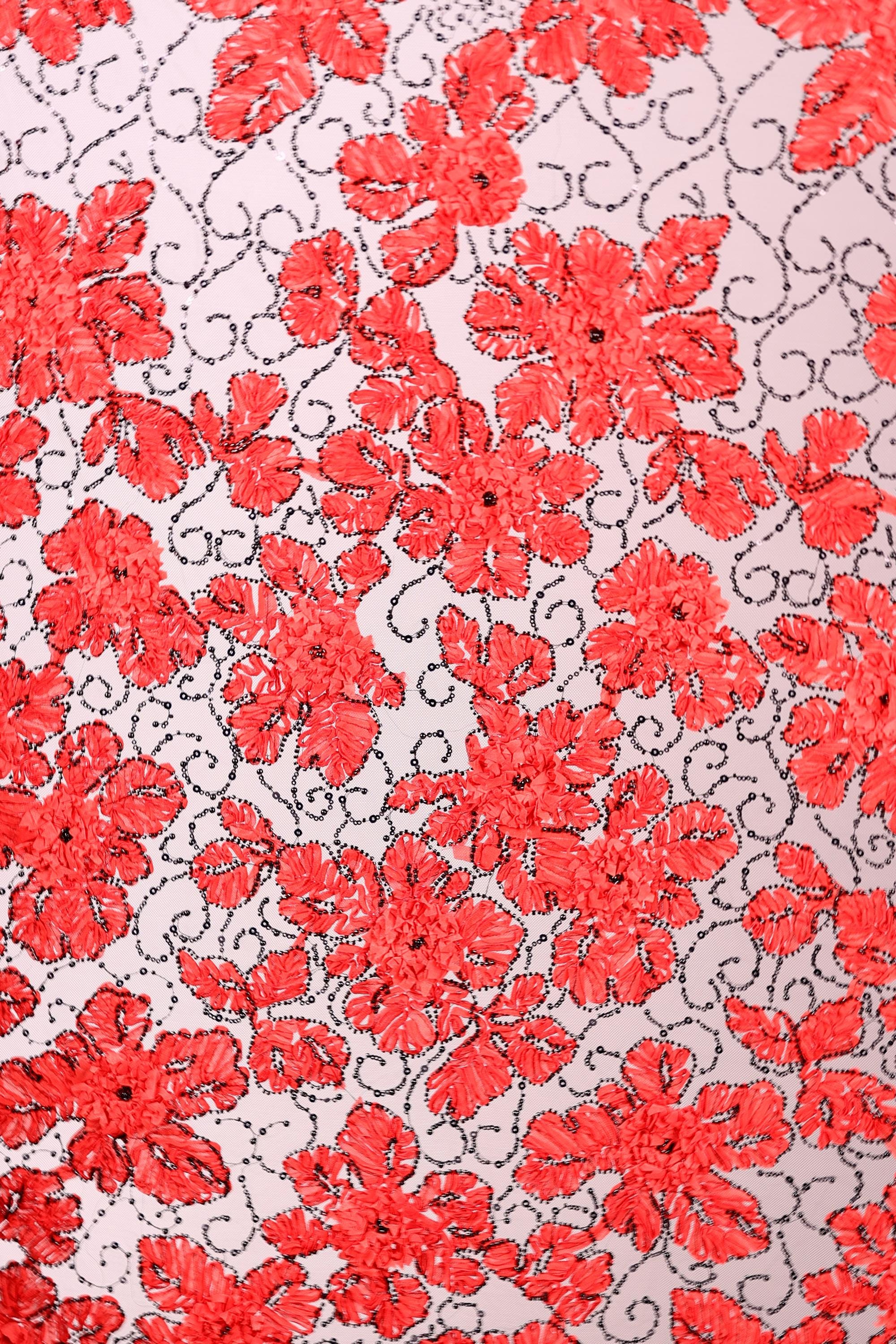 a close-up view of a fabric with a repeating pattern of red flowers and leaves. The flowers are the main focus of the image, with their vibrant red color and intricate details creating a visually striking pattern. The leaves, which are also red, are scattered throughout the fabric, adding to the overall floral design. The image does not contain any text or other discernible objects, and the focus is solely on the floral pattern.