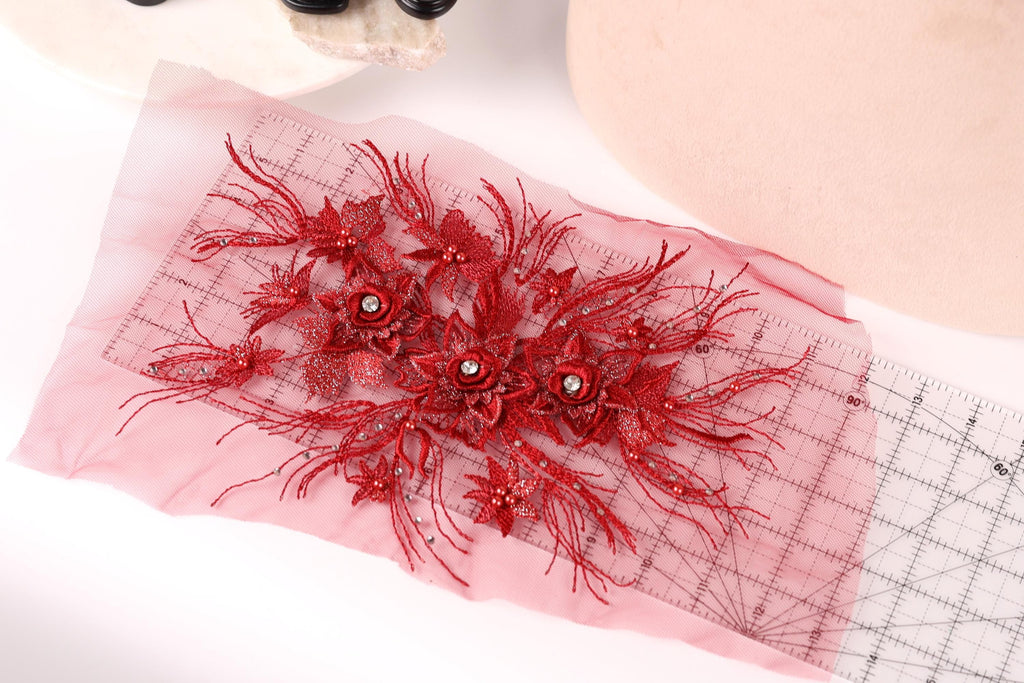 a close-up view of a red floral embroidery on a pink fabric, with a ruler and a pair of shoes visible in the background.