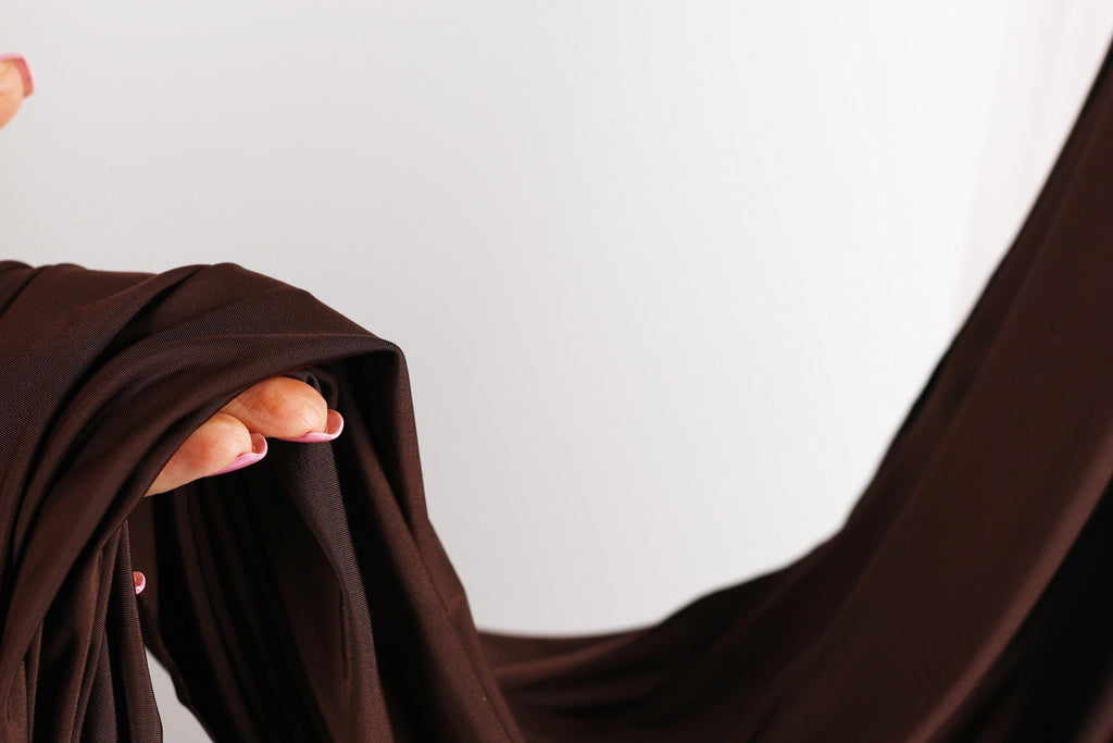 A hand holding a brown fabric, with the fingers curled and the palm facing upwards.