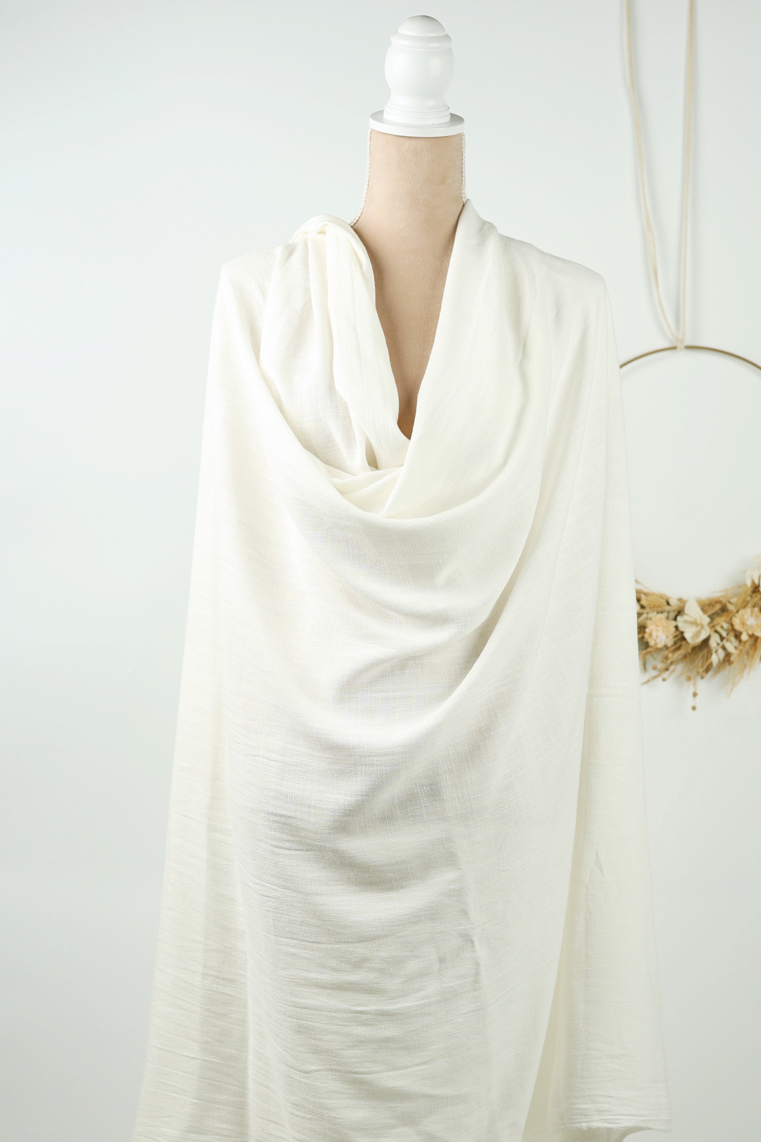 A mannequin wearing a white, flowing garment is displayed against a white background.