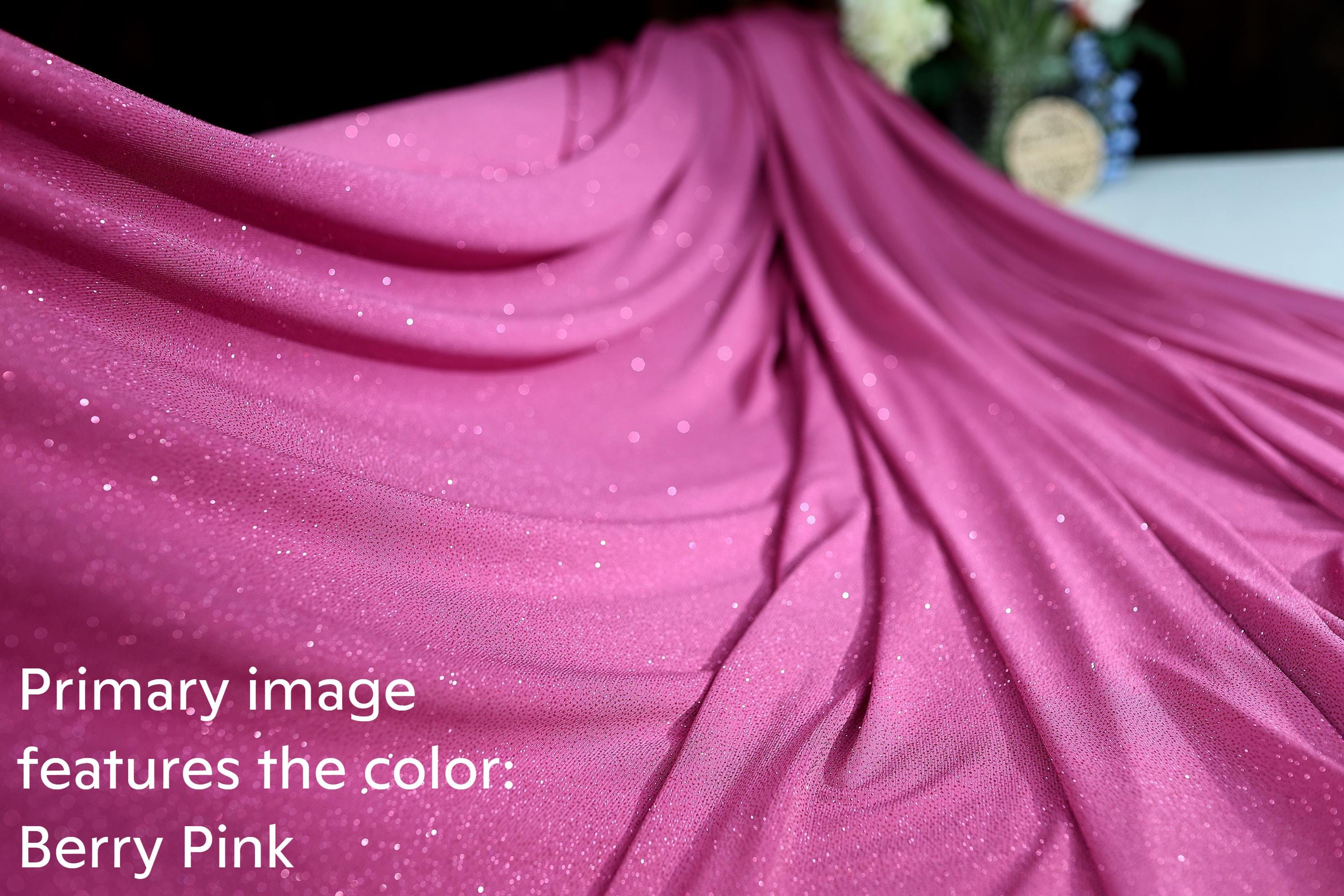 A close-up view of a shiny, pink fabric with a sparkly texture, likely a type of sequin or glittery material.