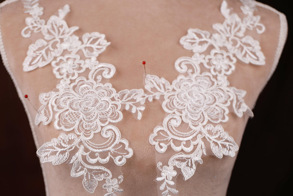 A close-up view of a mannequin torso wearing a white lace dress with intricate floral embroidery.