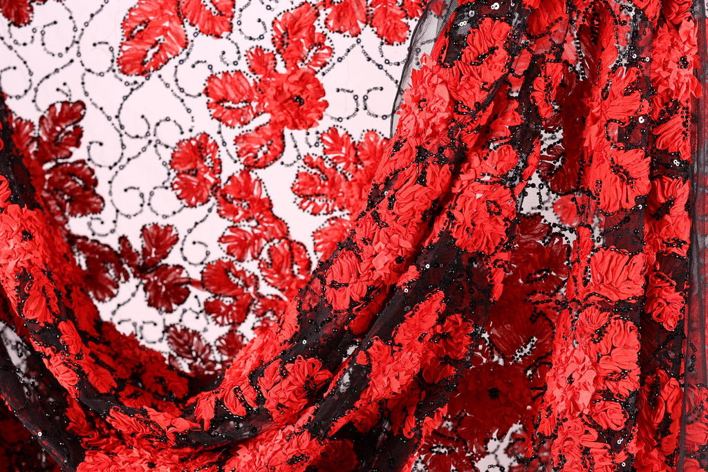 a close-up view of a fabric with a striking red floral pattern. The fabric appears to be made of a sheer material, with a black and red color scheme. The fabric is folded and draped, creating a visually appealing and intricate design.