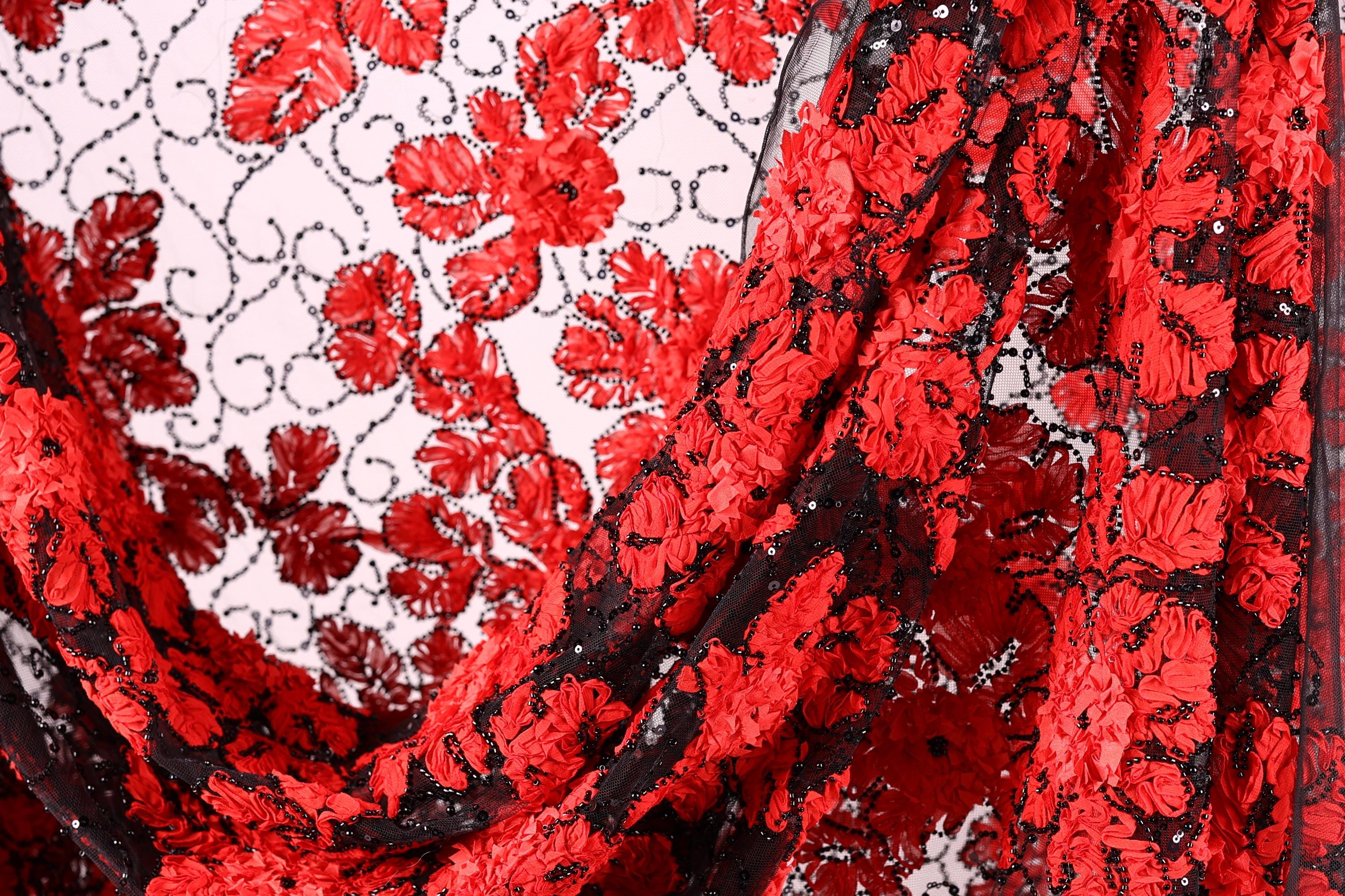 a close-up view of a fabric with a striking red floral pattern. The fabric appears to be made of a sheer material, with a black and red color scheme. The fabric is folded and draped, creating a visually appealing and intricate design.