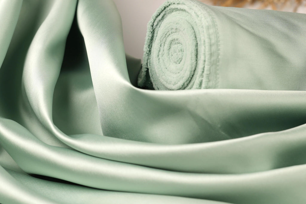 A close-up view of a piece of green satin fabric, with a rolled-up end visible.