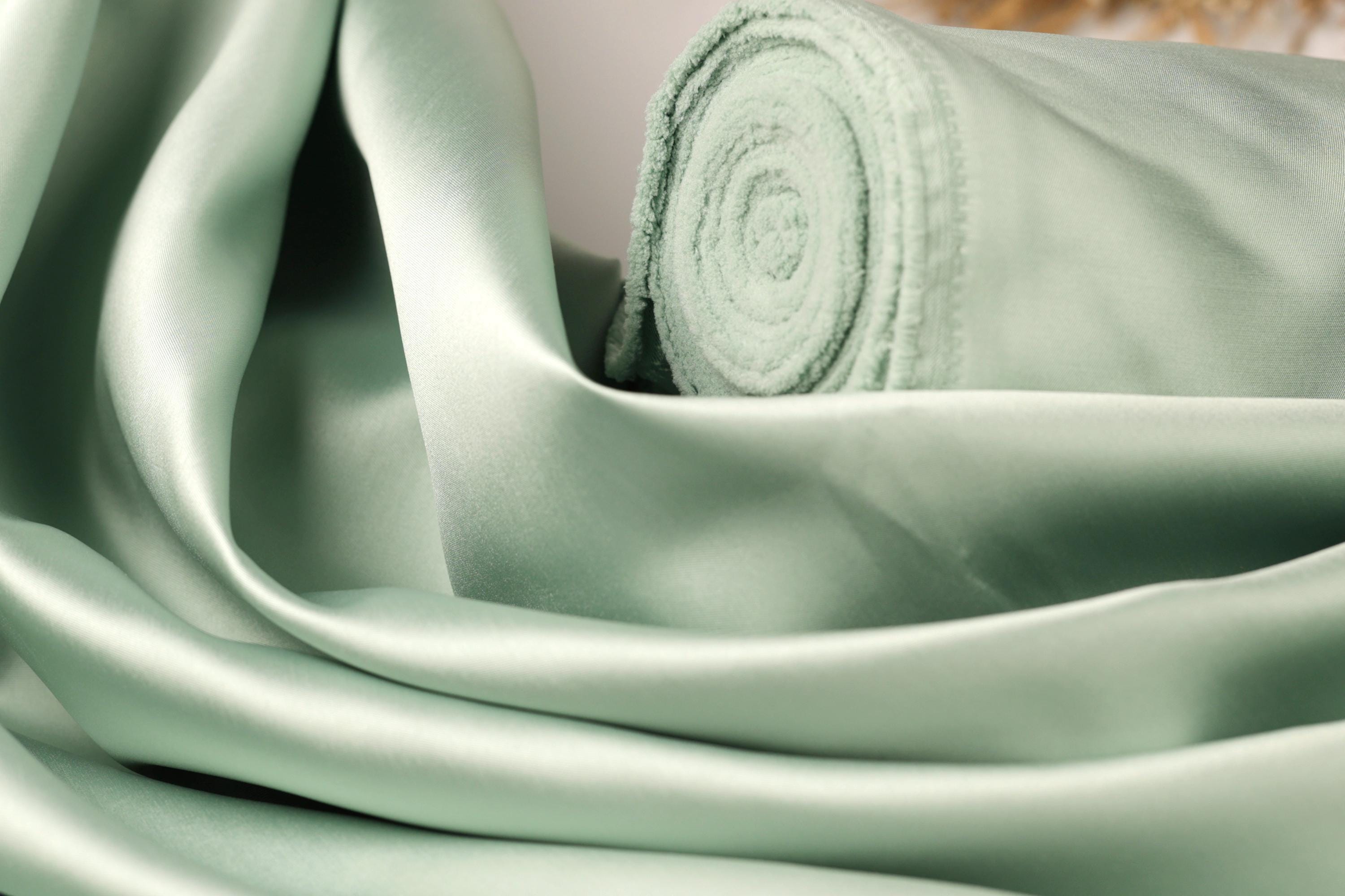 A close-up view of a piece of green satin fabric, with a rolled-up end visible.