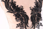 a close-up view of a delicate, intricate black lace design with floral and leaf-like patterns. The lace appears to be made of a shiny, black material and is embellished with small, round beads or sequins that add a touch of sparkle and elegance to the design.