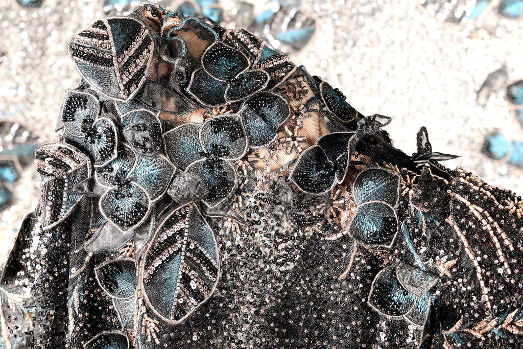 The image is a close-up of a black and blue sequined dress with intricate floral and leaf designs.