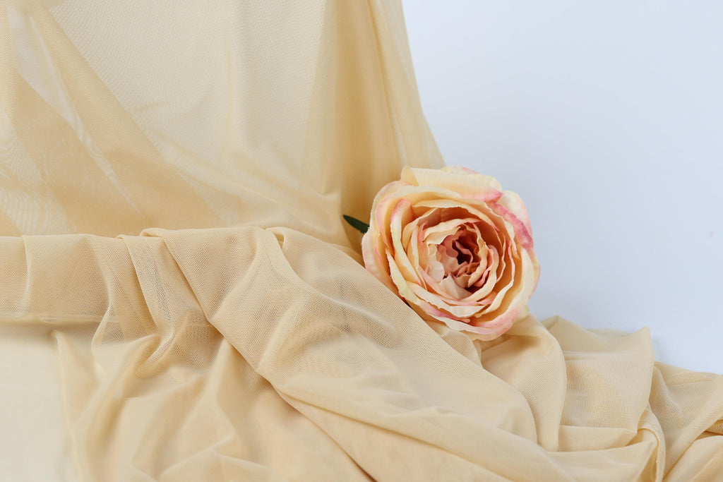 A single, vibrant pink rose rests on a crumpled beige fabric, creating a visually striking contrast.