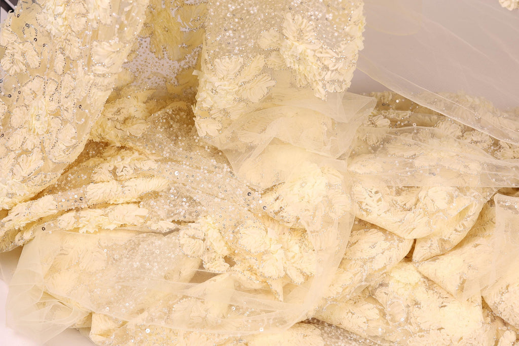 The image is a close-up of a delicate, white fabric with intricate embroidery and lace-like patterns. The fabric appears to be a sheer, sheer-like material, possibly a sheer veil or a sheer dress. The image does not contain any text or other discernible objects, and the focus is solely on the fabric's texture and design.