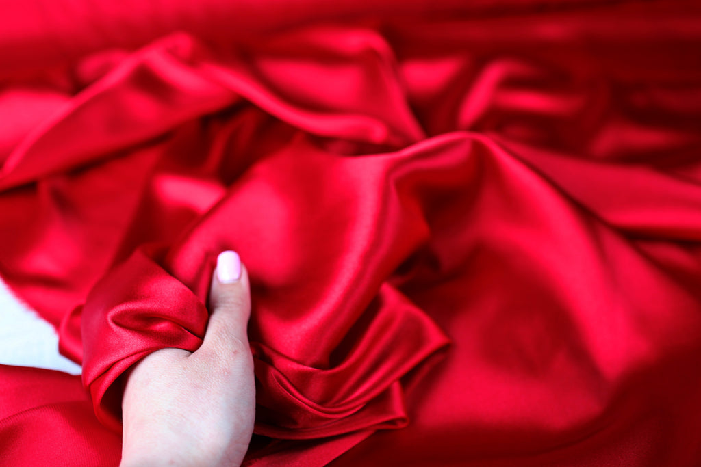 A hand is holding a piece of red satin fabric, which appears to be soft and smooth.