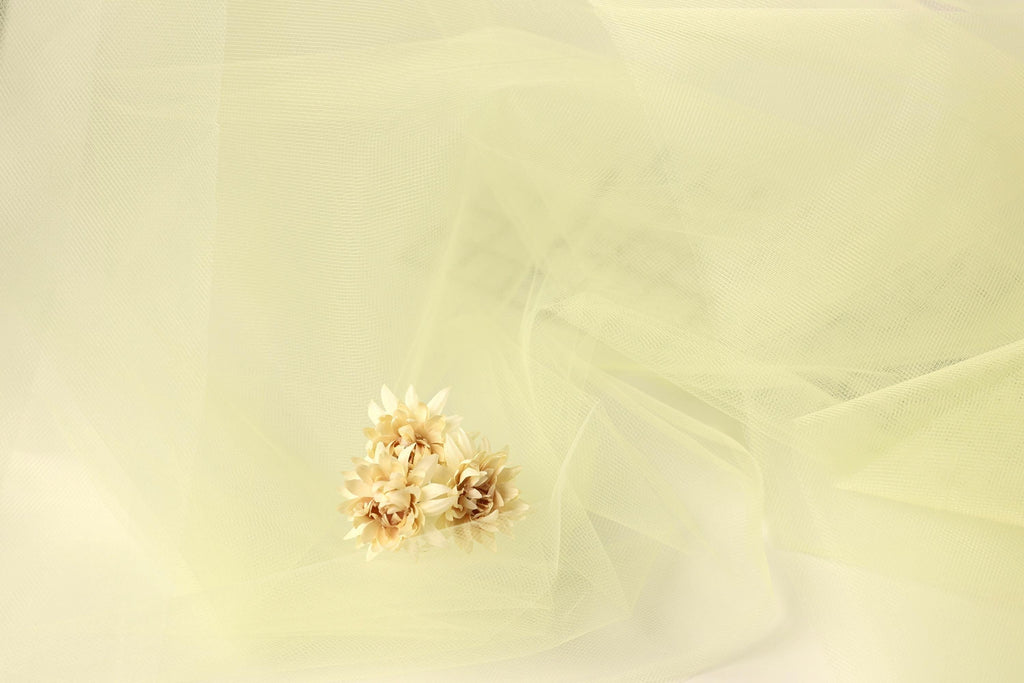 A single delicate flower is the focal point of the image, set against a soft, light yellow background.