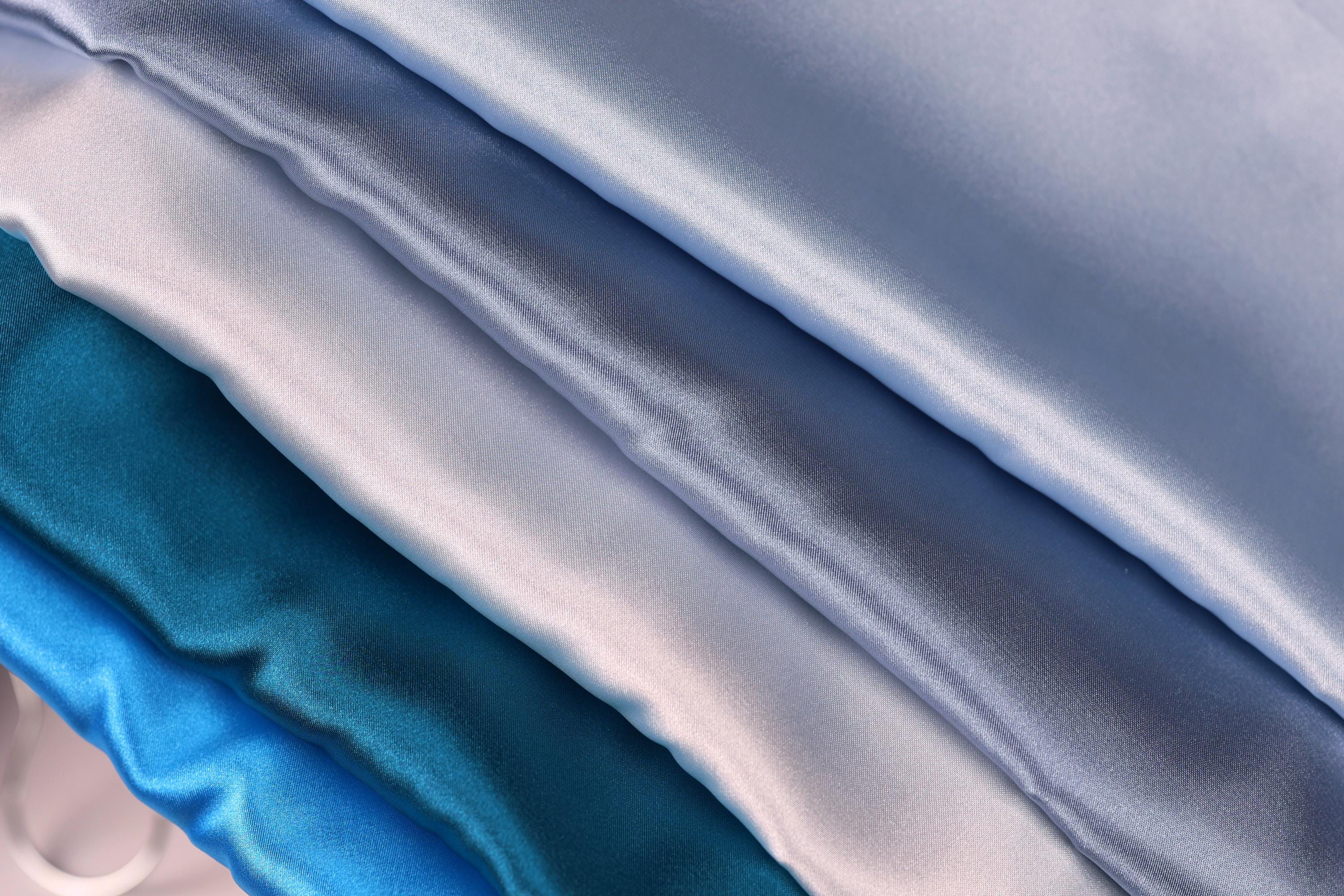 a close-up view of several layers of shiny, silky fabric in various shades of blue, ranging from light to dark.
