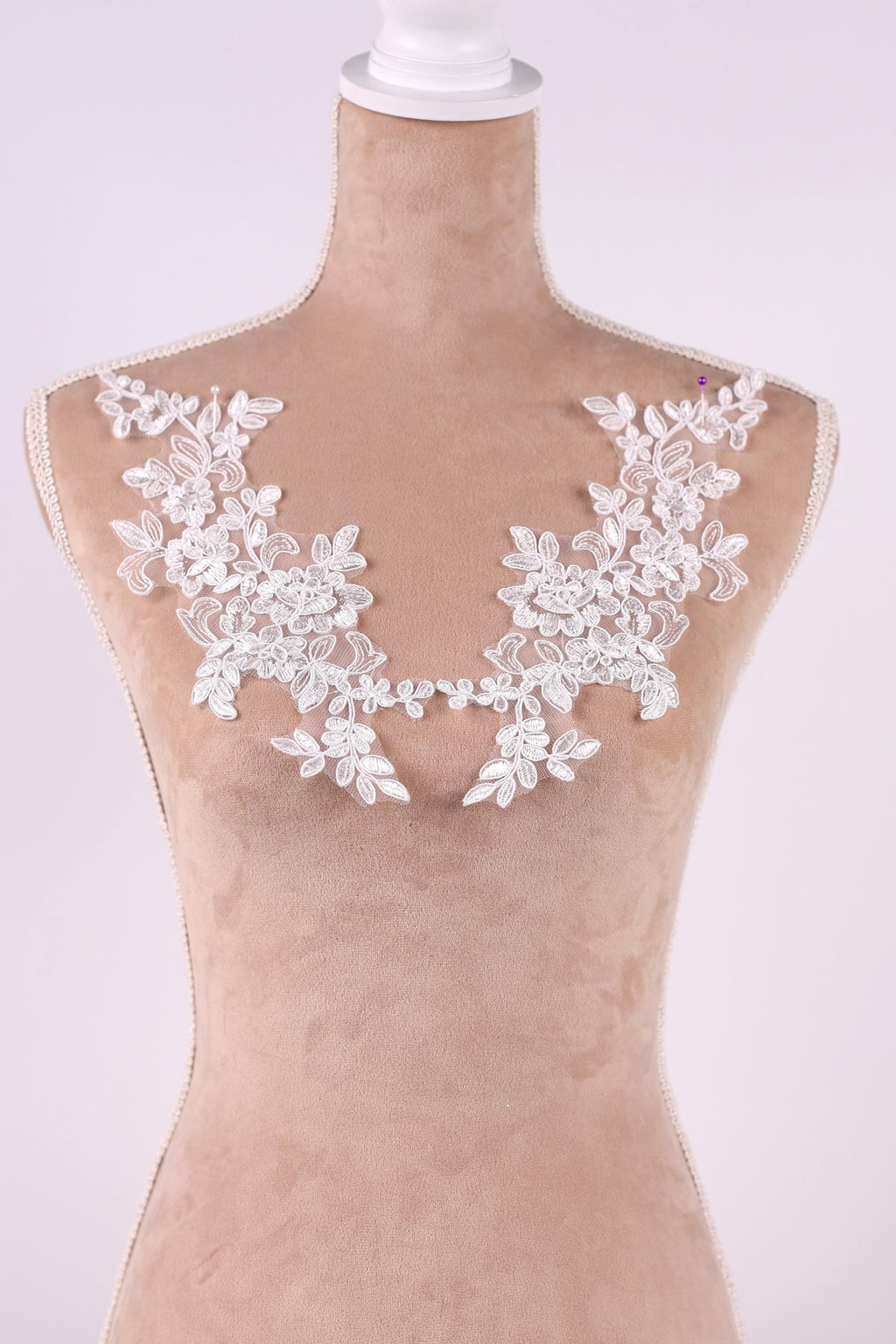 A mannequin wearing a beige dress with white lace flowers on the shoulders.