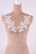 A mannequin wearing a beige dress with white lace flowers on the shoulders.