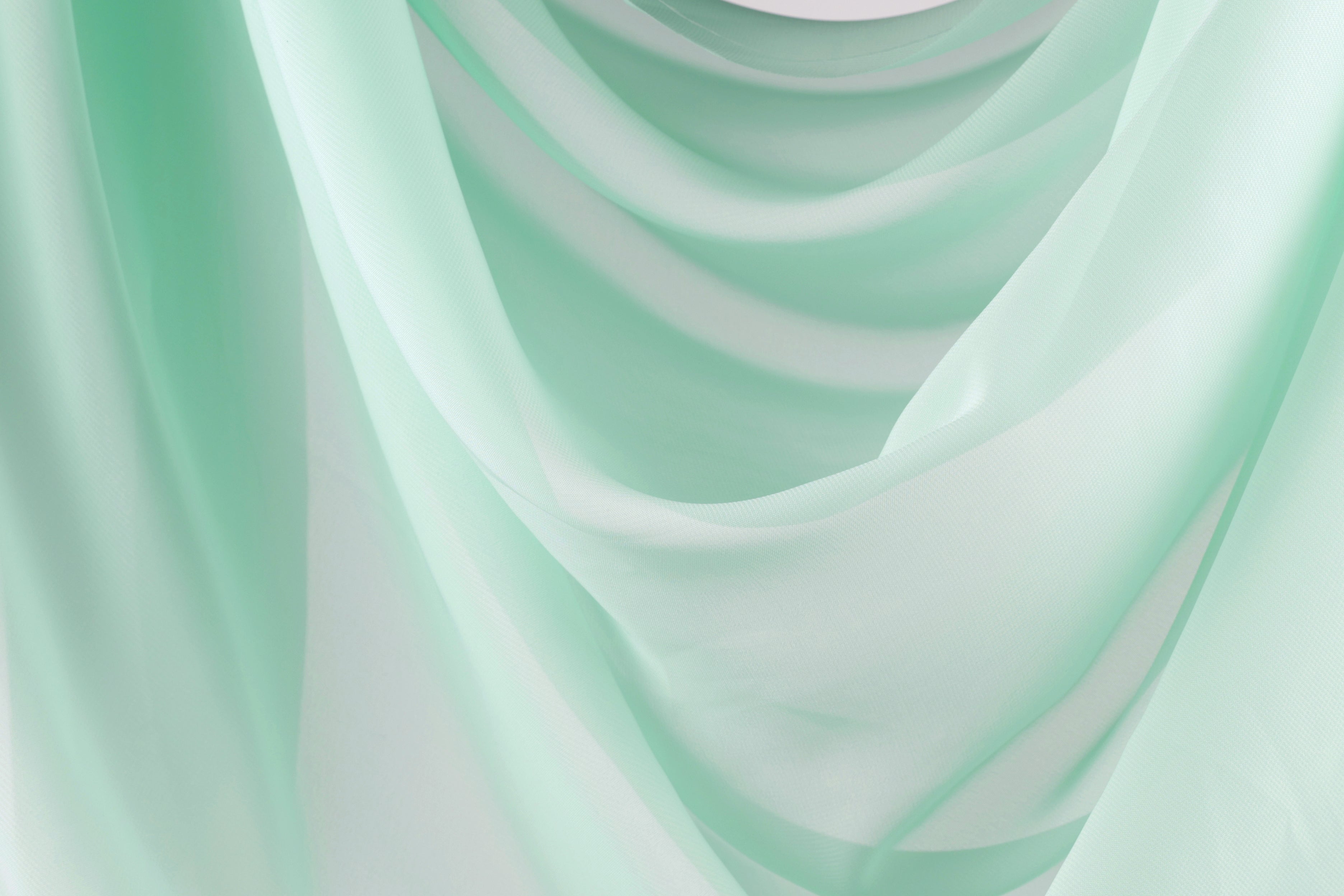 The image is a close-up of a light green fabric, possibly a sheer or sheer-like material, with a soft, flowing texture. The fabric appears to be draped or draped over a surface, creating a sense of movement and softness.
