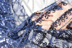 A close-up view of a hand holding a piece of blue and black sequined fabric, with the fabric's intricate patterns and textures visible.