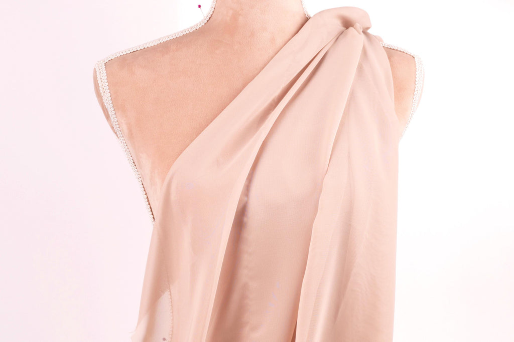A mannequin wearing a light pink draped fabric draped over its shoulder.