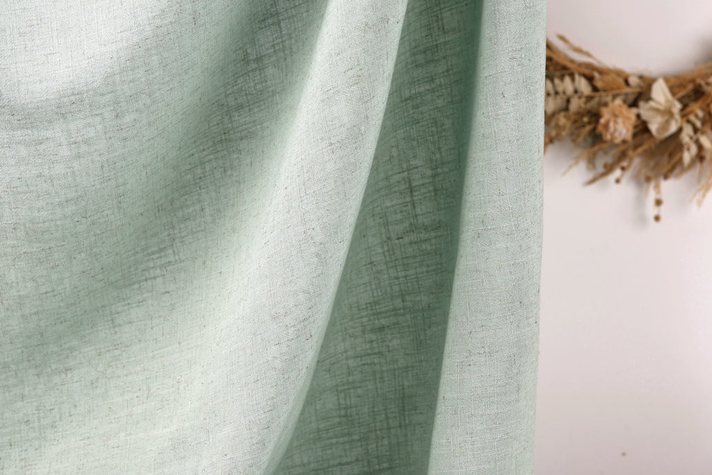 a close-up view of a light green fabric, possibly a curtain or textile, with a wreath of dried flowers or branches visible in the background.