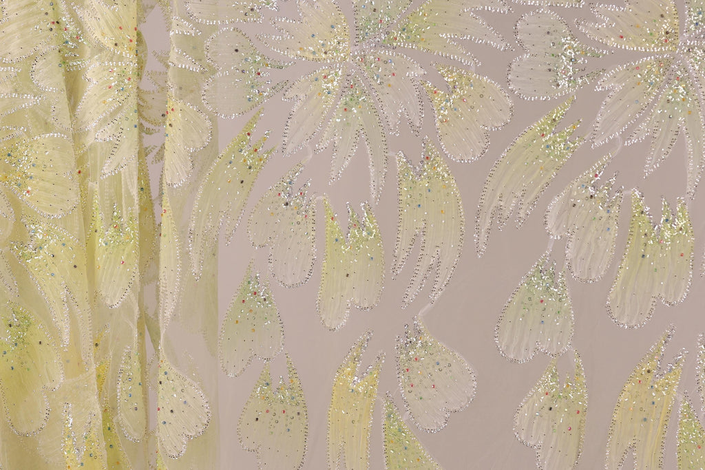 a close-up view of a fabric with a floral pattern, including yellow and white flowers with sparkles. The fabric appears to be a sheer material, possibly a sheer dress or garment.