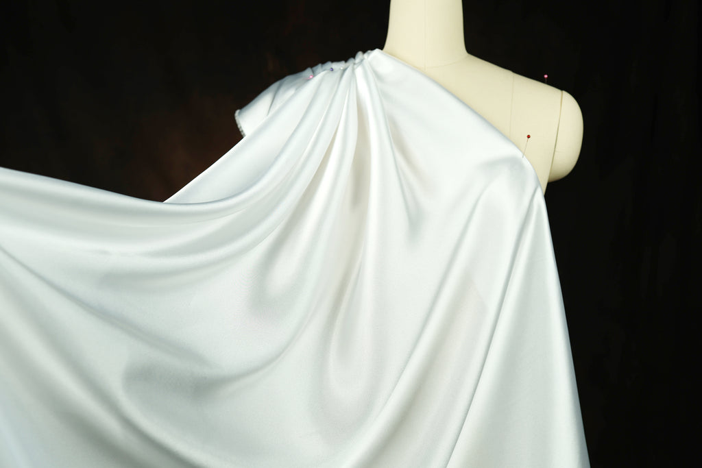 A mannequin wearing a white satin garment with a flowing, draped appearance.