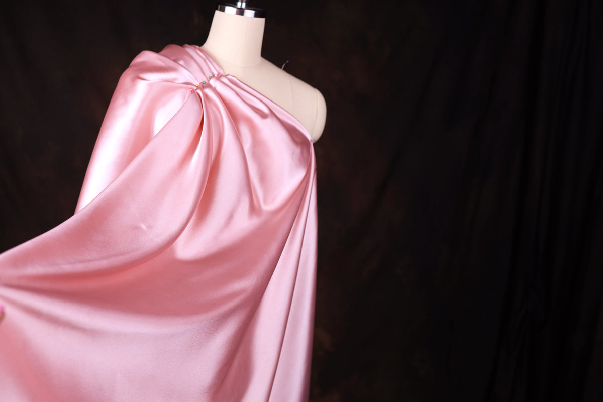 A mannequin wearing a pink satin one-shoulder dress against a dark background.