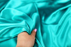 A hand is holding a piece of turquoise fabric, with the fabric appearing to be soft and smooth.