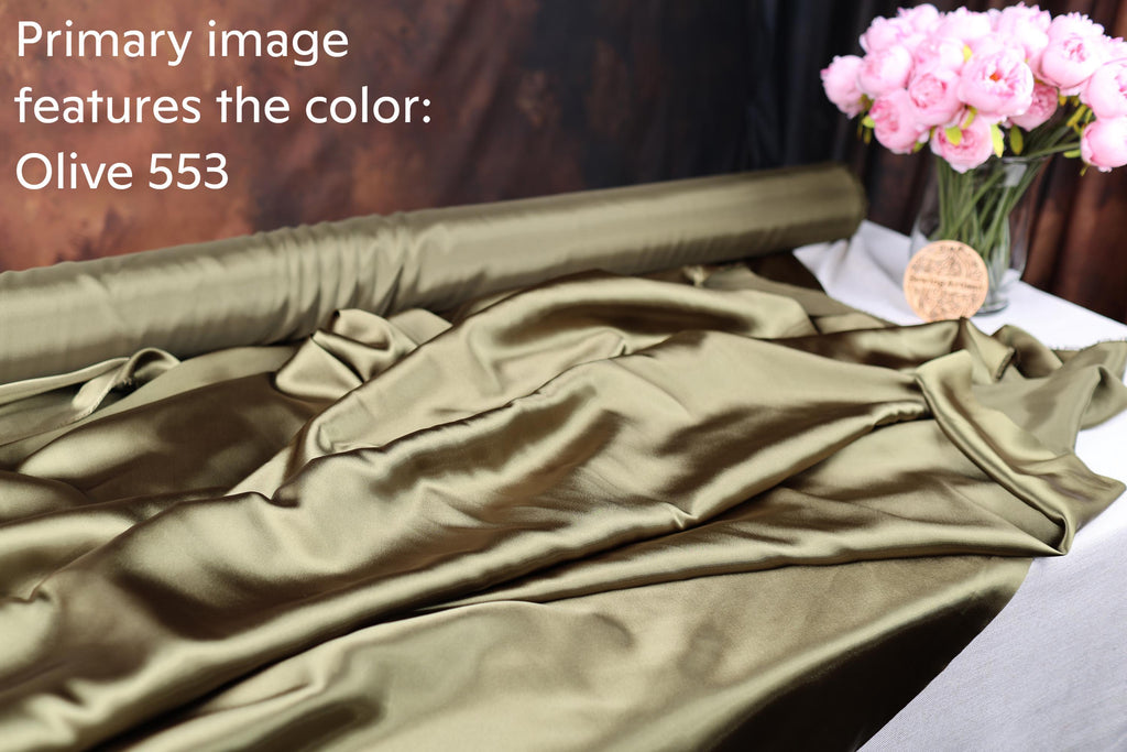 a roll of olive green satin fabric and a vase of pink flowers on a table.
