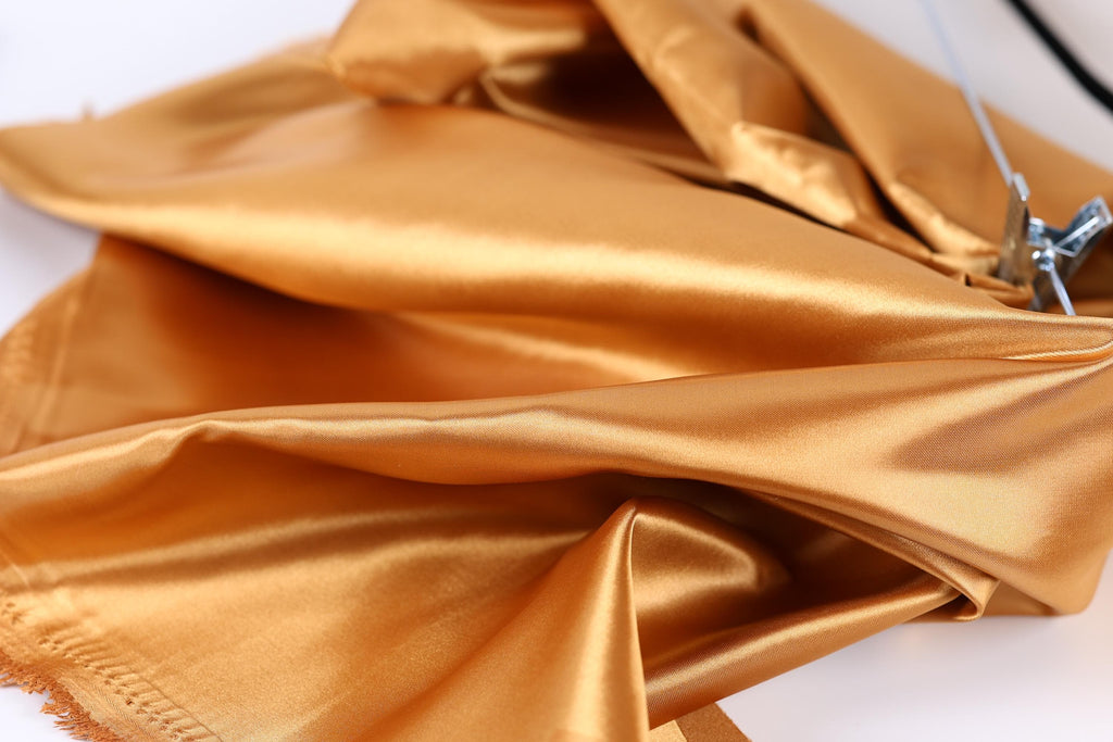 a close-up view of a shiny, golden-colored fabric, possibly silk or satin, with a metallic clip attached to it.