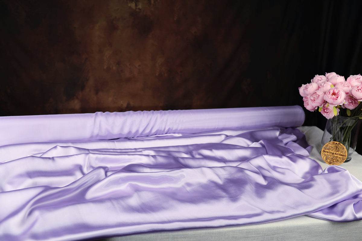a large roll of purple satin fabric, a vase of pink roses, and a dark brown background.