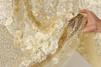 A hand is holding a piece of fabric with a gold sequin and flower pattern, which appears to be a decorative piece of clothing or textile.