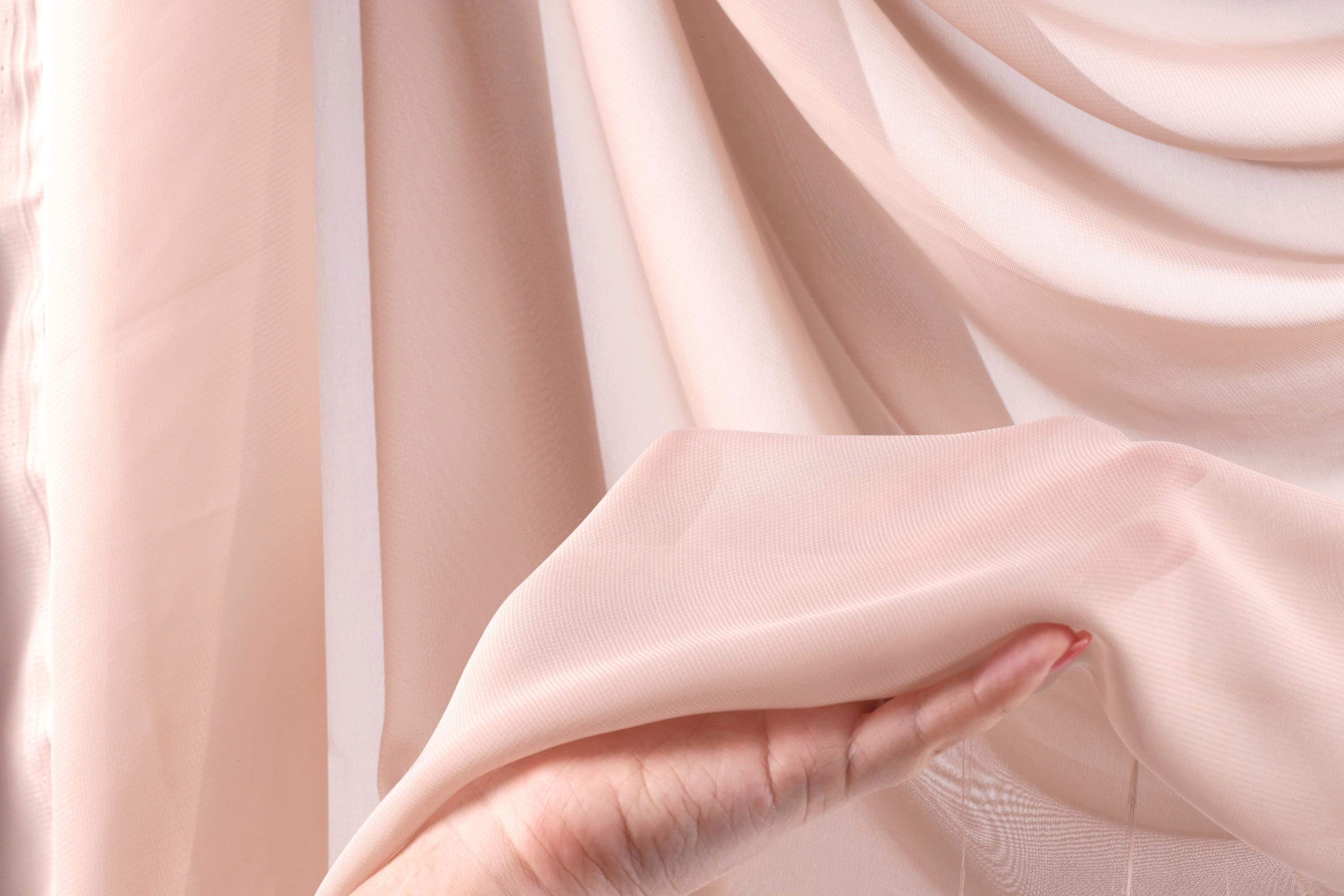 A hand is holding a piece of light pink fabric, which appears to be a sheer or sheer-like material.