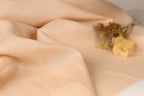 a close-up view of a soft, light-colored fabric, possibly a piece of linen or a similar material. In the background, there are a few yellow flowers, including a single yellow flower in the center and two more flowers on the right side of the frame.