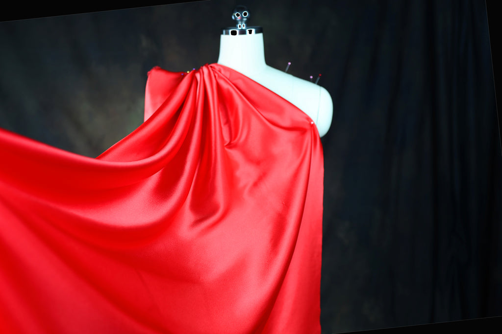 A mannequin wearing a red satin dress with a flowing, draped design.