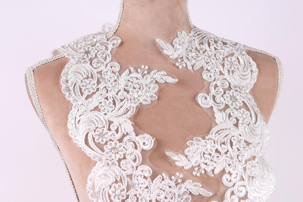 A close-up view of a mannequin wearing a white lace dress with intricate floral patterns.