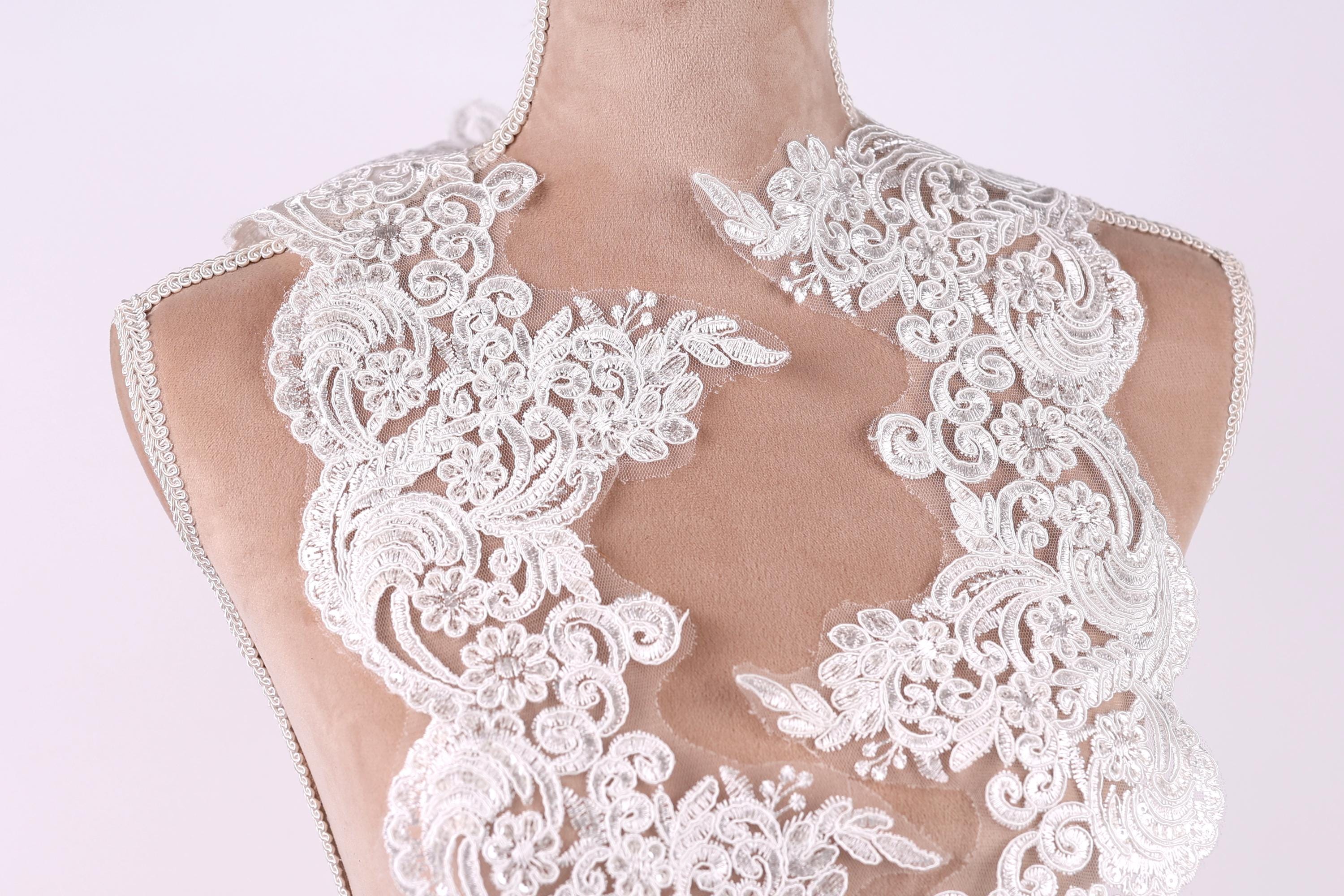 A close-up view of a mannequin wearing a white lace dress with intricate floral patterns.