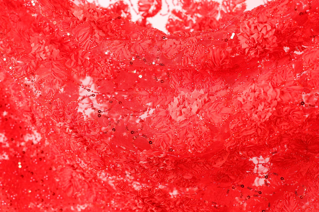 The image is a close-up of a red fabric with a floral pattern, featuring small black sequins or beads scattered throughout the fabric.