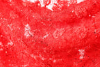 The image is a close-up of a red fabric with a floral pattern, featuring small black sequins or beads scattered throughout the fabric.