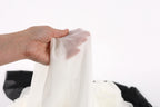 A hand is holding a white fabric, possibly silk or chiffon, against a plain white background.