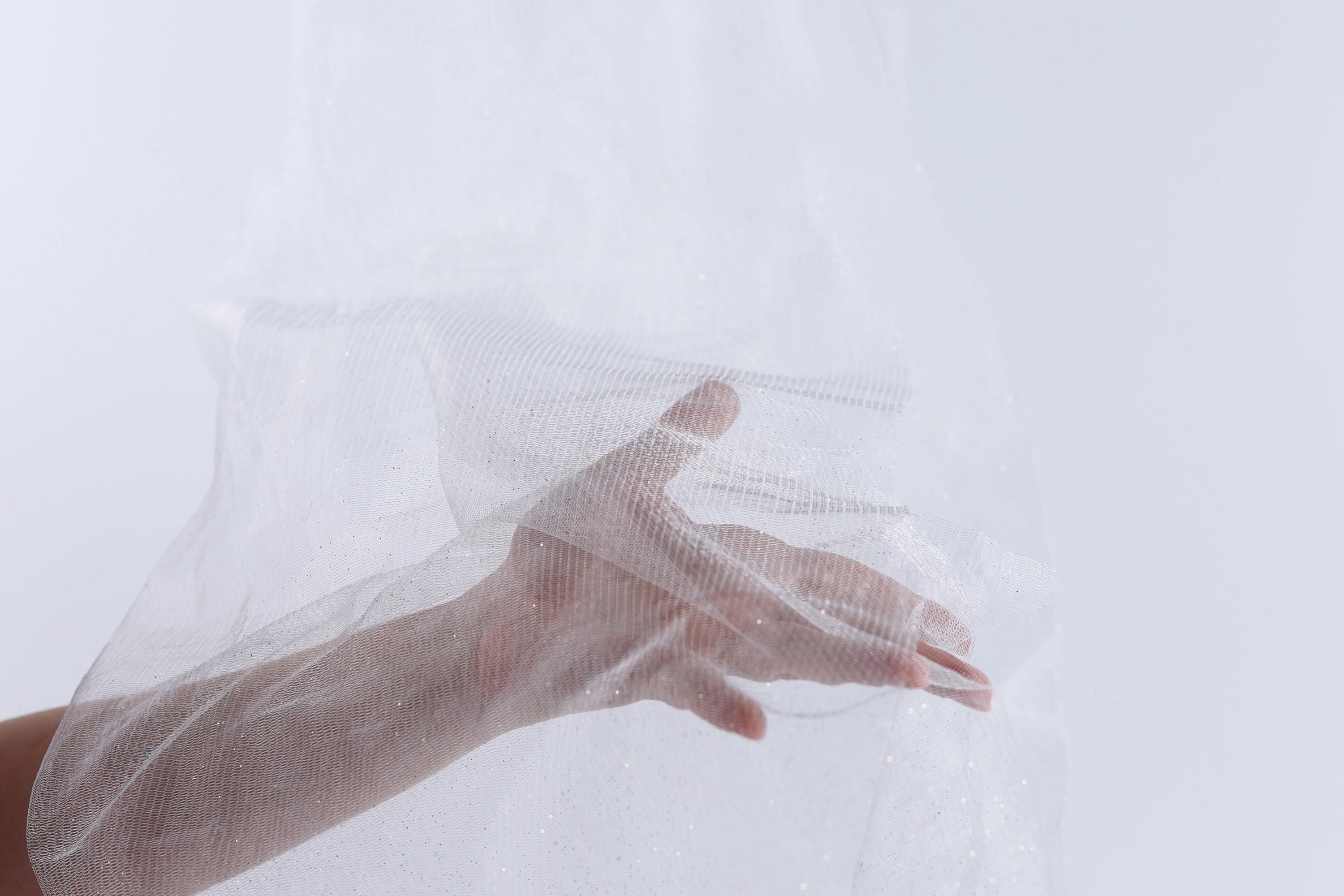 A hand is holding a white, transparent fabric or veil, which appears to be made of a sheer material.