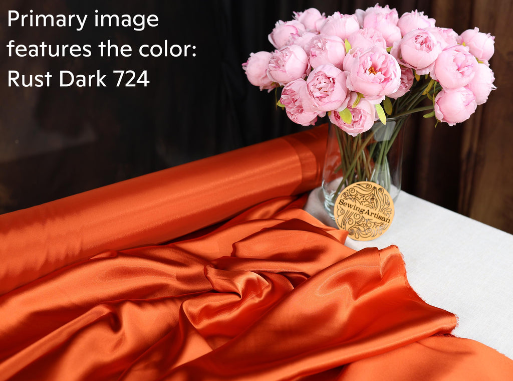 a bouquet of pink flowers in a vase, placed on a table with a roll of orange fabric and a small gold-colored object.